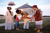 Un interprète montre une ceinture métisse à un jeune visiteur. / Photo: Parcs Canada.